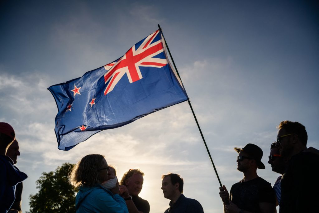A man raises a New Zealand flag. (Photo by Anthony WALLACE / AFP) (Photo by ANTHONY WALLACE/AFP via Getty Images)