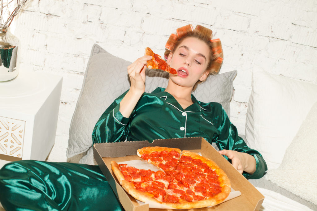young sexy lazy woman in pajamas lying in bed and eating big pizza