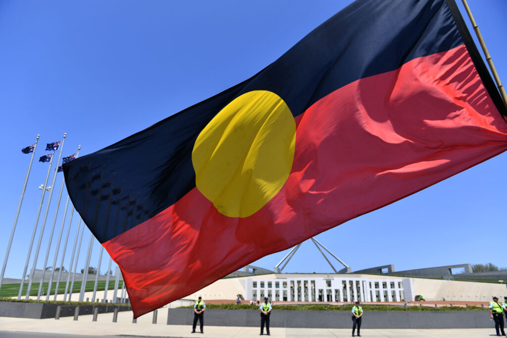 A marcher holds a flag as he protests for Aboriginal rights on Australia Day at Parliament House in Canberra, Sunday, January 26, 2020. (AAP Image/Mick Tsikas) NO ARCHIVING